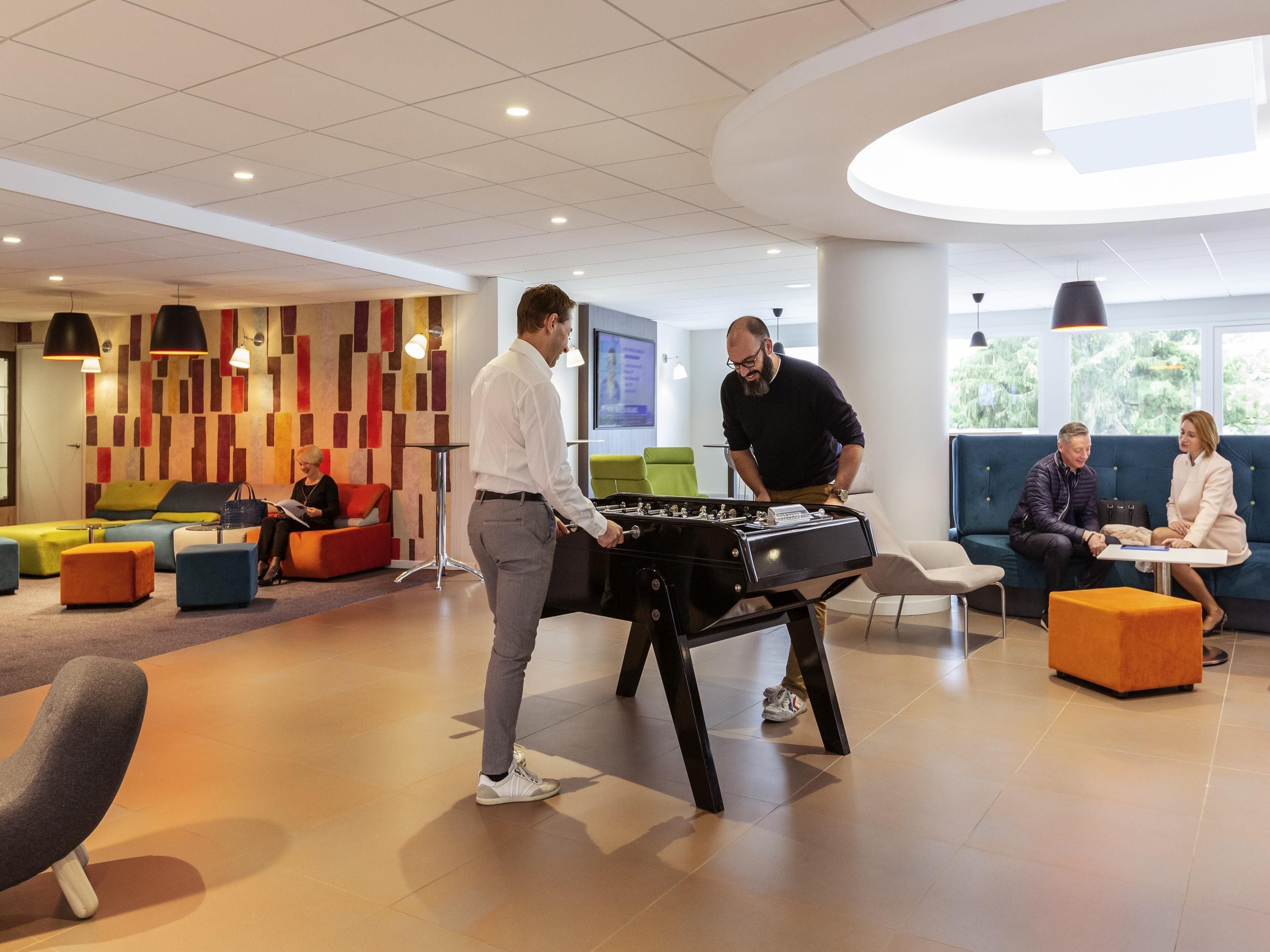A modern lobby with seating areas, a foosball table, and a large window providing a view of greenery.