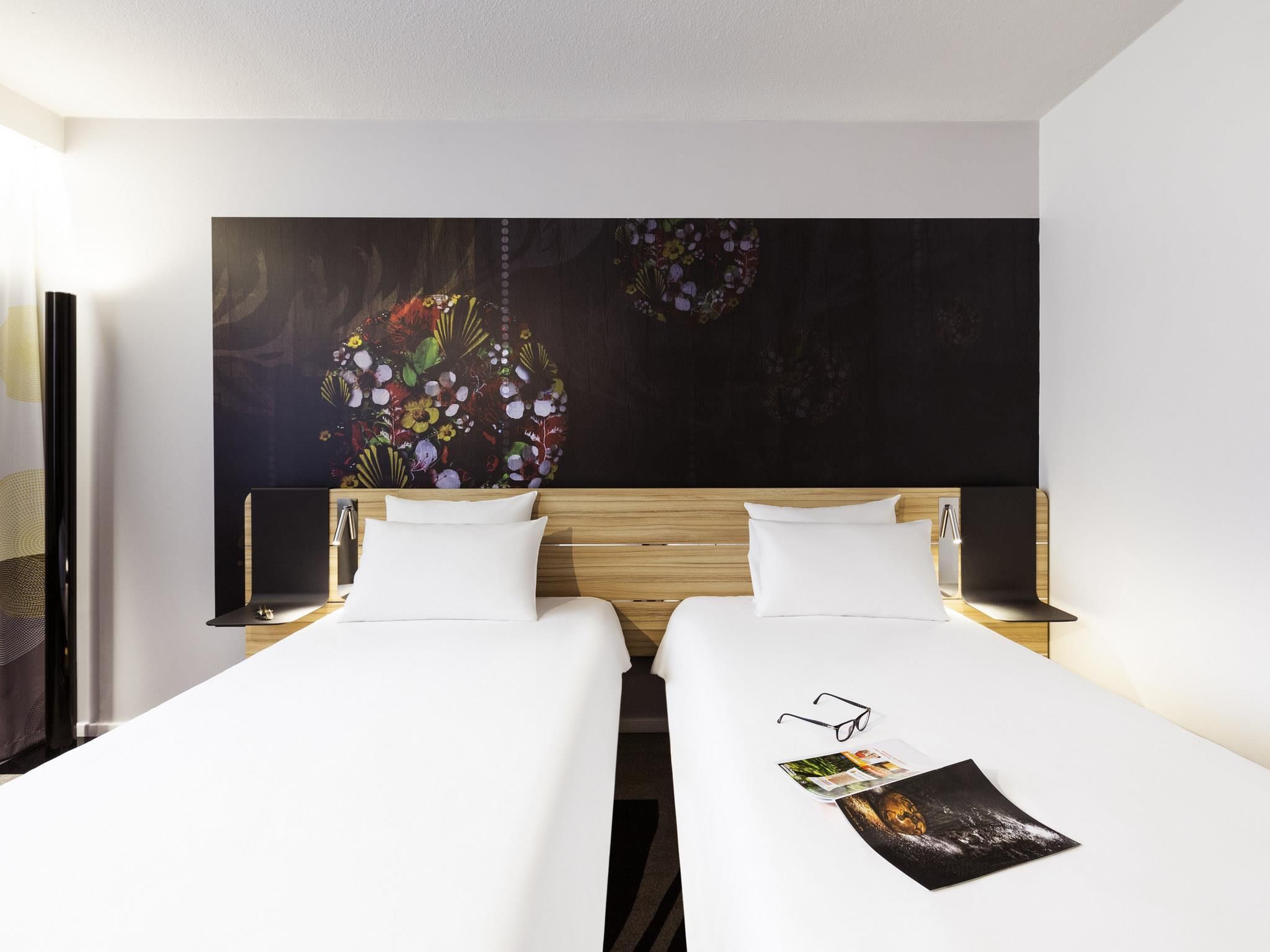 Una habitación de hotel con dos camas, una obra de arte floral grande en la pared y una revista sobre la cama.