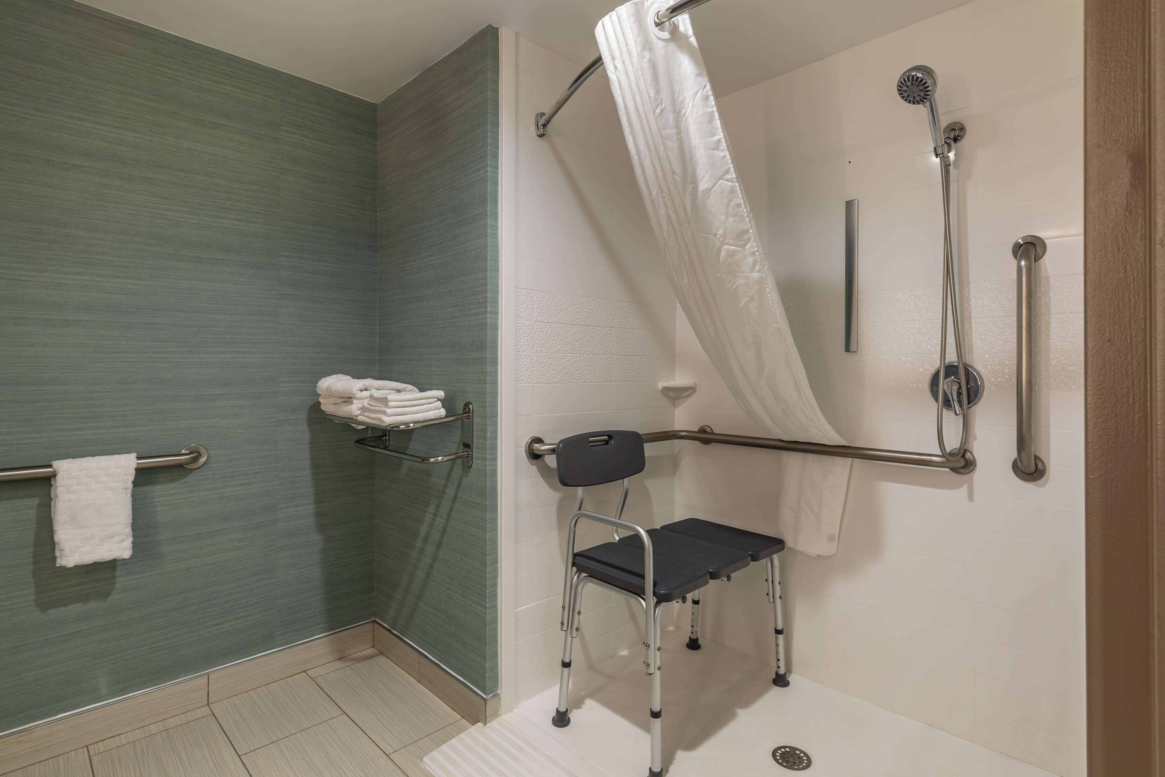 A bathroom with a shower, grab bars, a wheelchair-accessible bench, and a towel rack.