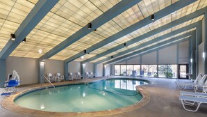 Una piscina interior con techo azulejado, sillones de descanso y vistas al exterior.