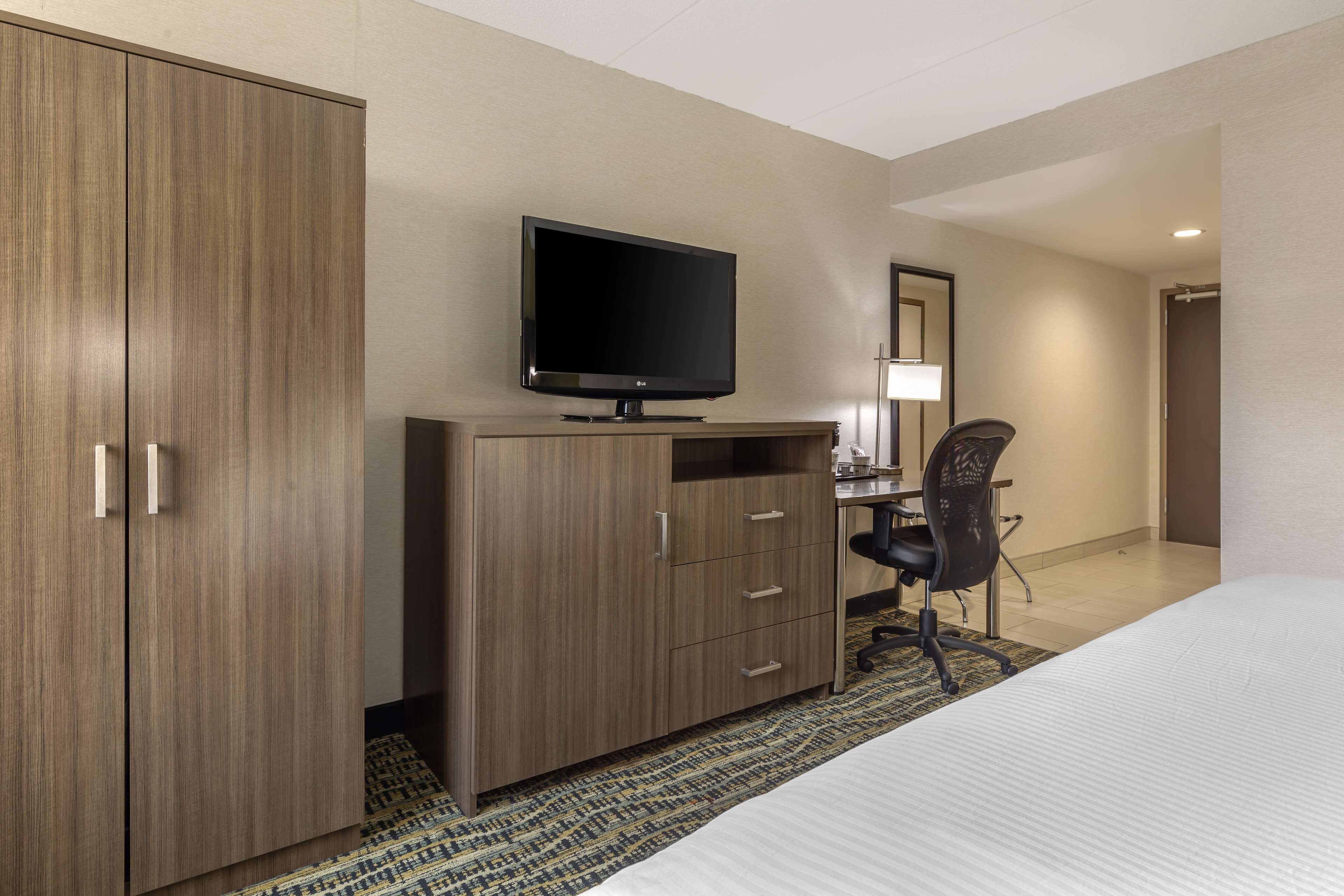 A hotel room with a bed, a desk with a computer, a television, and a wardrobe.