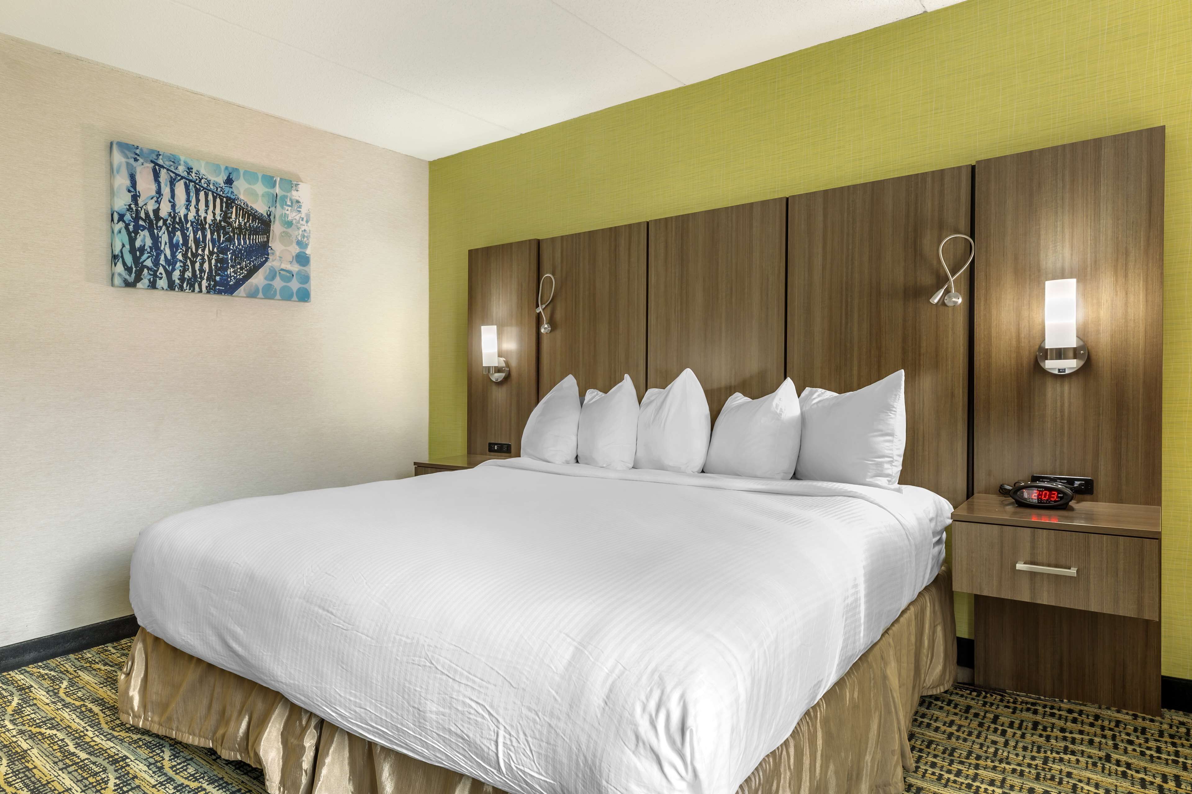 A hotel room with a large bed, a wooden headboard, two bedside tables with lamps, and a wall-mounted clock.