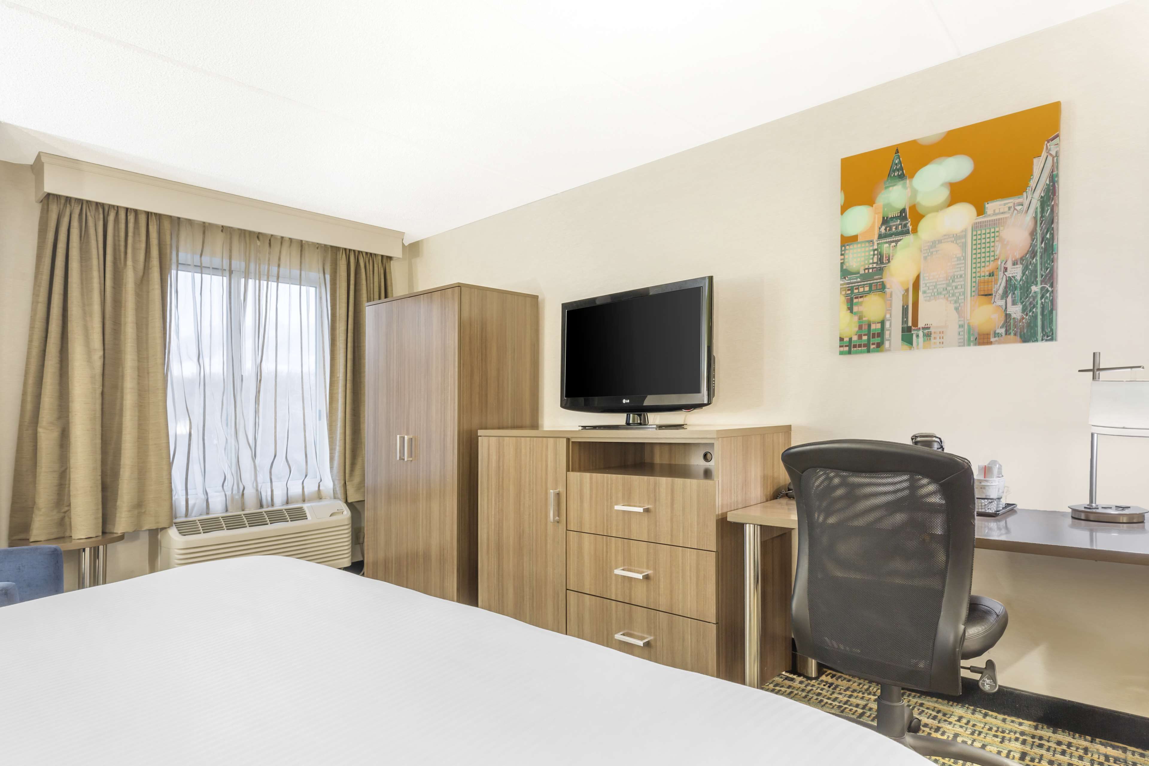 Une chambre d’hôtel avec un lit, un bureau avec un ordinateur, une chaise, une télévision et un tableau au mur.