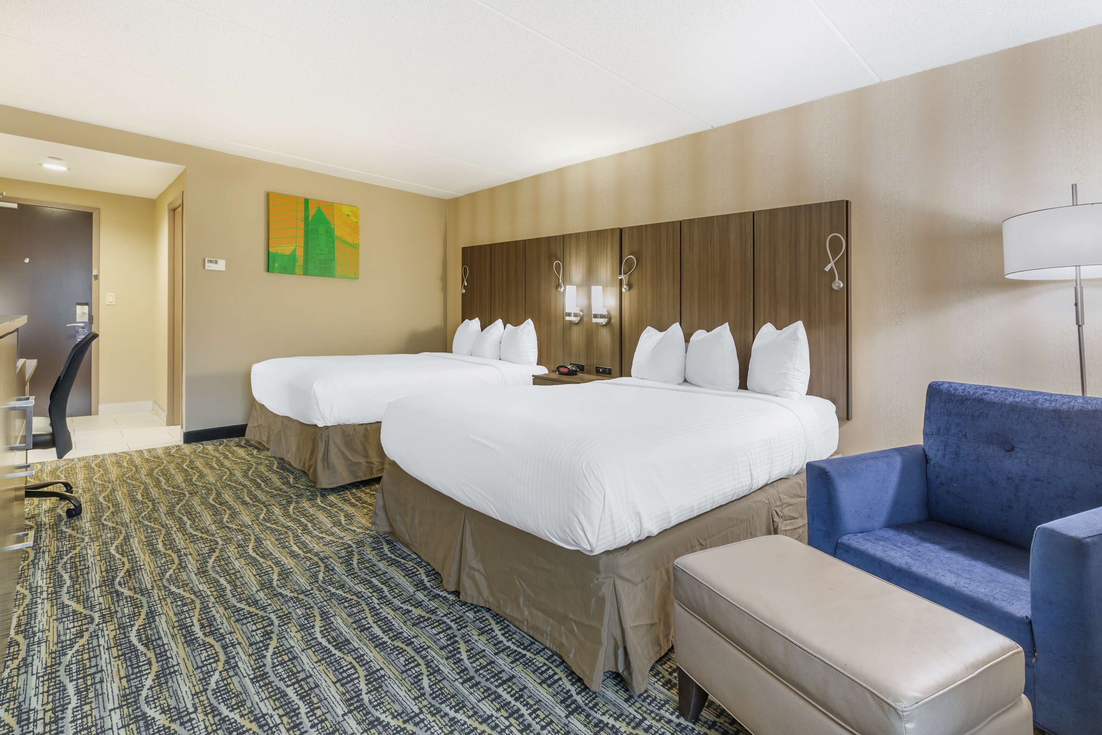 A hotel room with two beds, a sofa, a desk, and a patterned carpet.