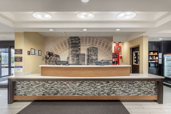 A hotel reception desk with a cityscape mural, a check-in counter, and a digital display.