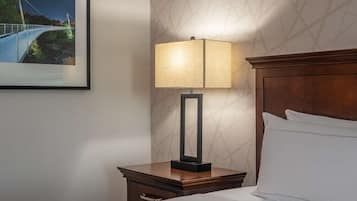 Une chambre d’hôtel bien rangée, avec un lit, une table de chevet dotée d’une lampe et un tableau encadré accroché au mur.