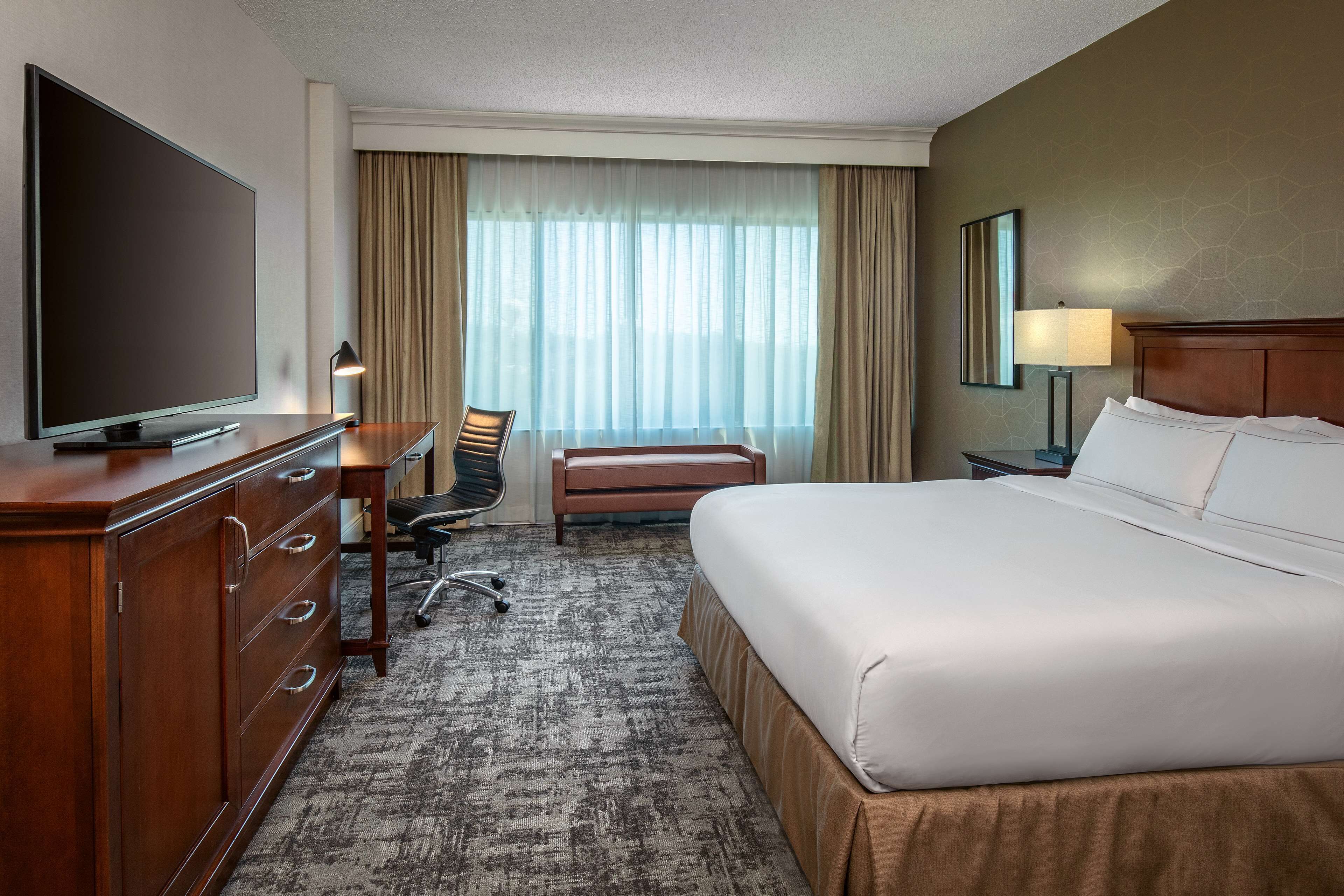 A hotel room with a large bed, a desk with a chair, a television, and a lamp.