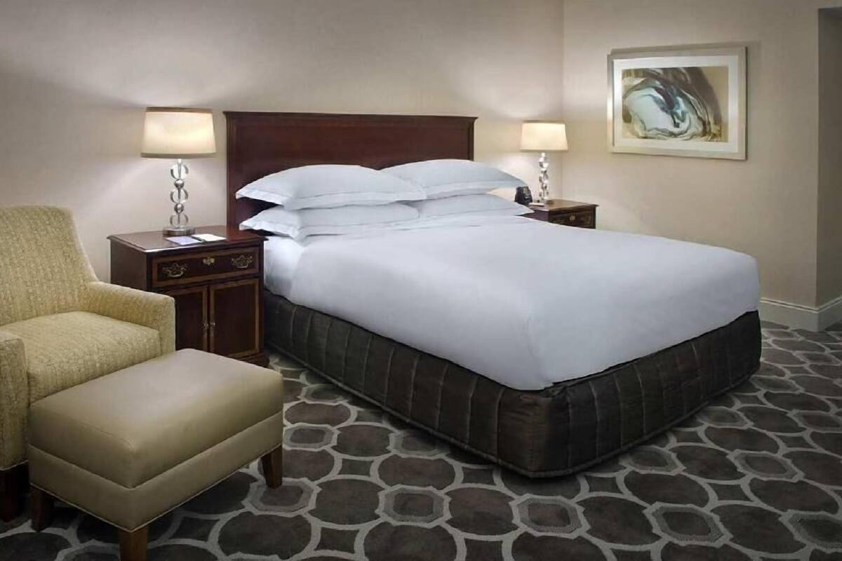 Une chambre d’hôtel avec un lit, deux tables de chevet avec des lampes, une chaise et un tapis à motifs.
