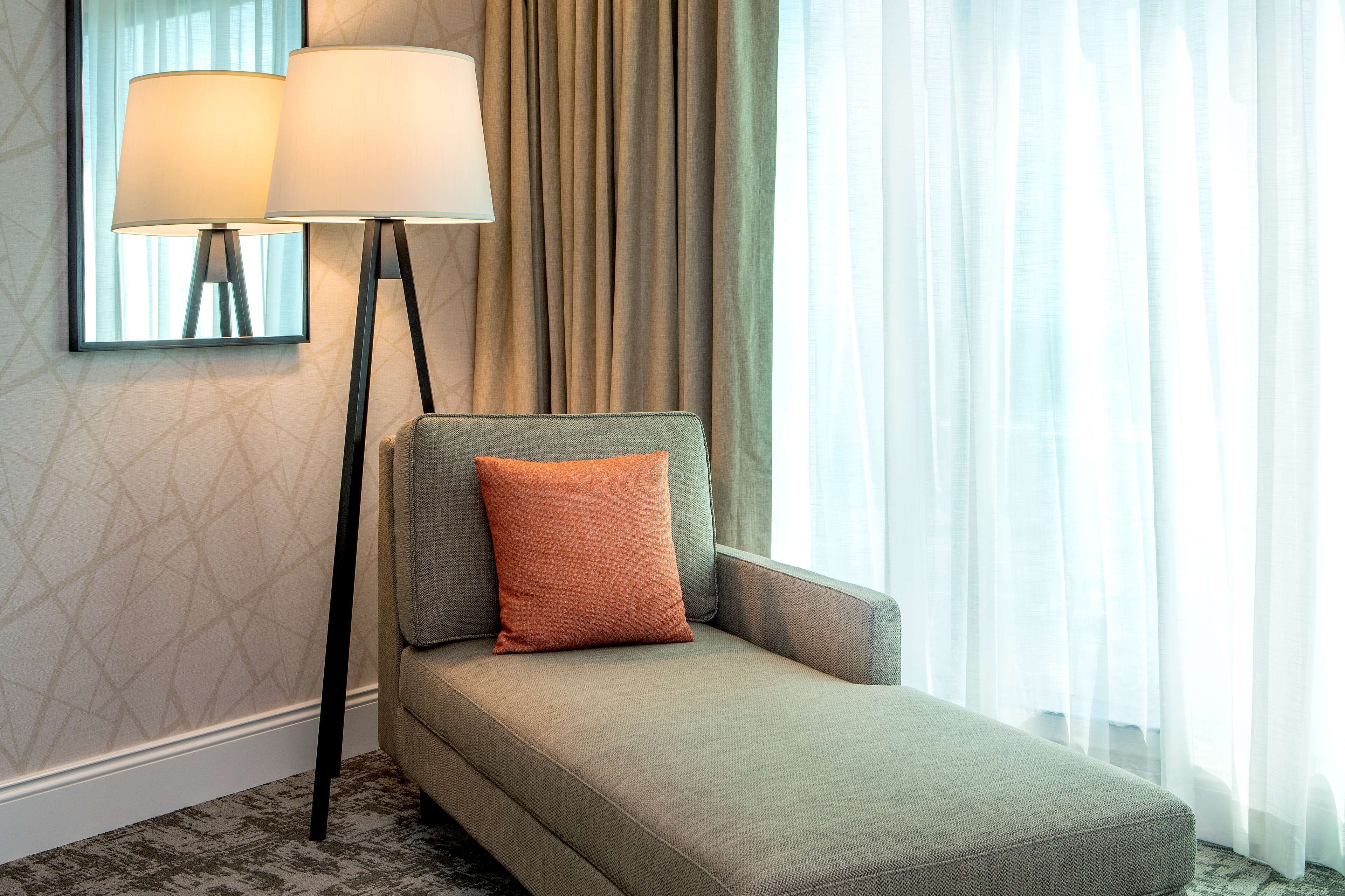 Una habitación de hotel moderna con un sofá, una lámpara de pie y cortinas translúcidas.