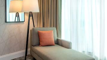 Una habitación de hotel moderna con un sofá, una lámpara de pie y cortinas translúcidas.