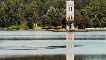 A tower with a clock on a lakeside property surrounded by trees.
