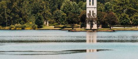 A tower with a clock on a lakeside property surrounded by trees.