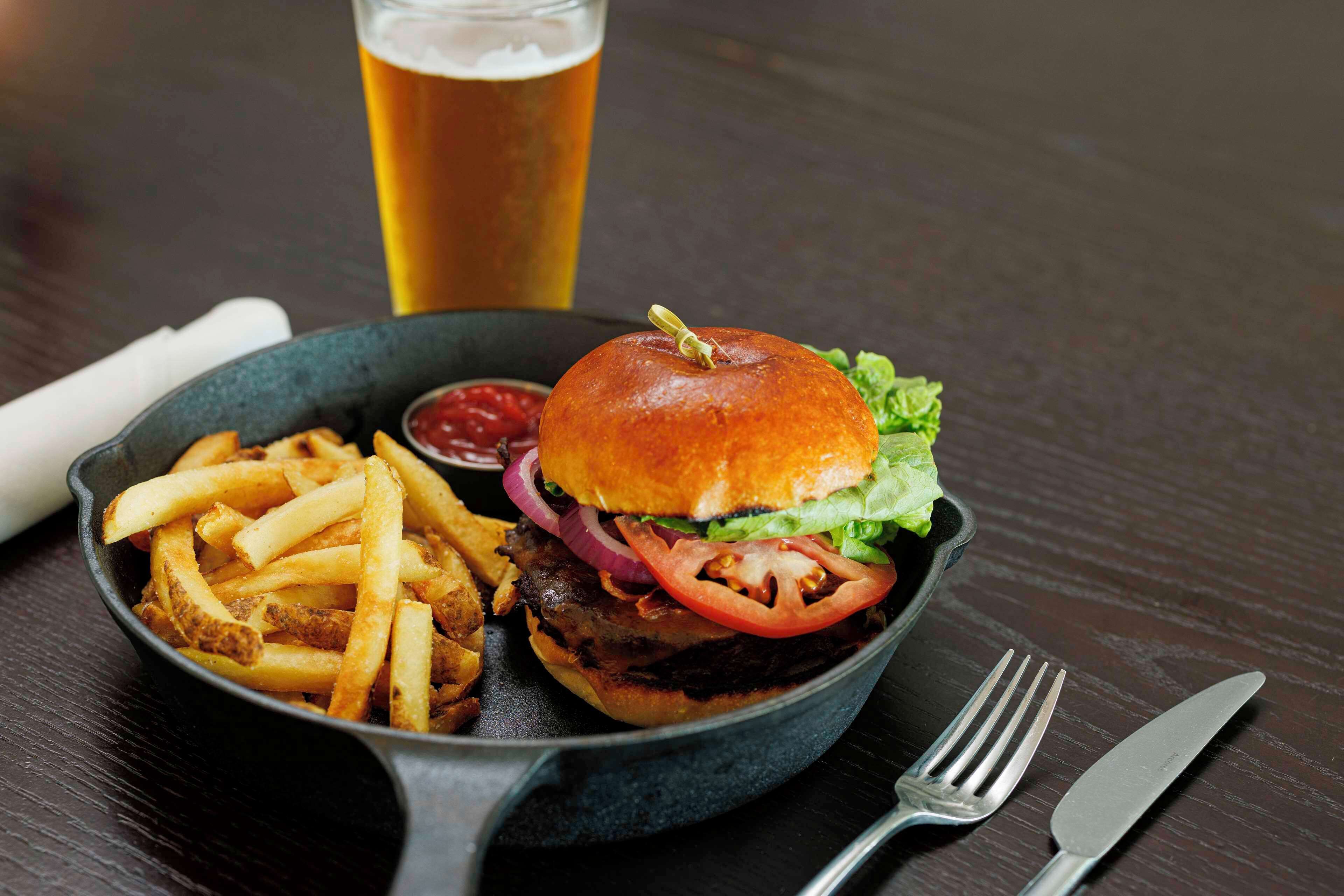 Un plato con una hamburguesa, papas fritas y una cerveza en una mesa de madera.