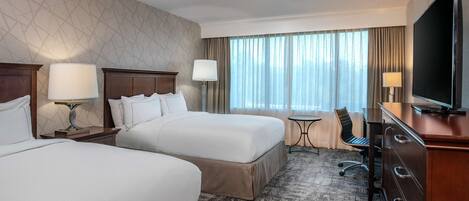 A hotel room with two beds, a desk, a chair, a TV, and a window with curtains.