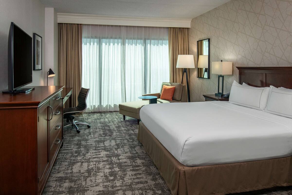 Une chambre d’hôtel avec un grand lit, un bureau avec une chaise, une télévision et une lampe.