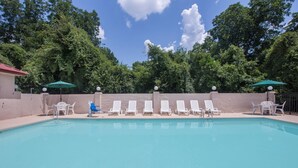 Une piscine entourée d’arbres, avec des chaises longues blanches et des parasols.
