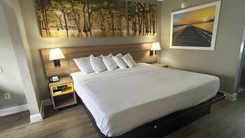 Habitación de hotel con una cama grande, dos lámparas de noche, una mesita de noche, un cuadro de un bosque y vistas al atardecer.