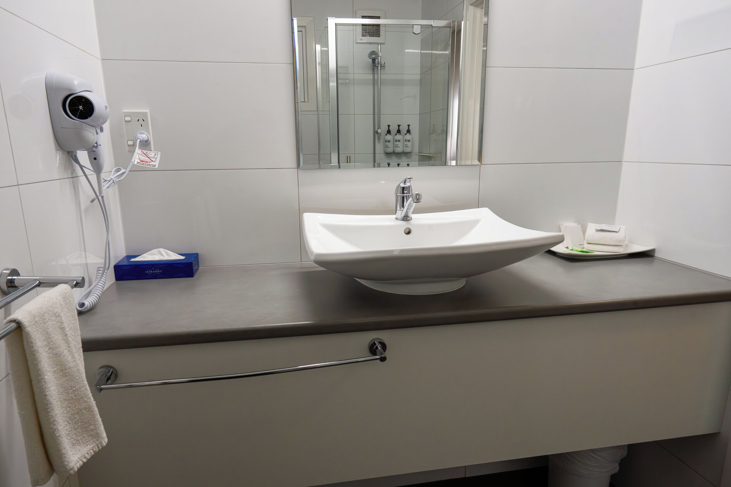 A bathroom with a white sink, a mirror, a towel rack, and a hairdryer on a wall-mounted outlet.
