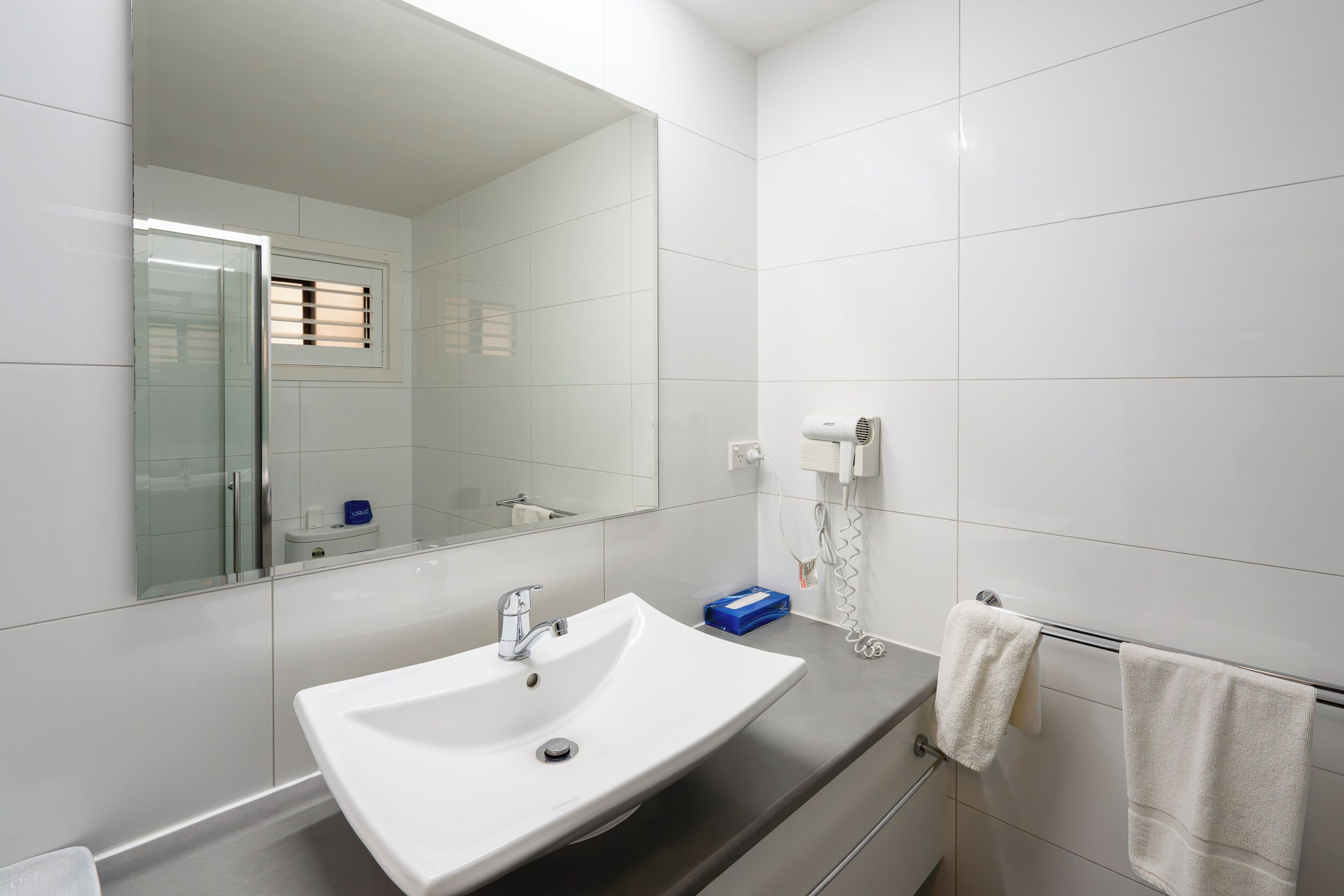 A modern bathroom with a white sink, a large mirror, and a towel rack.