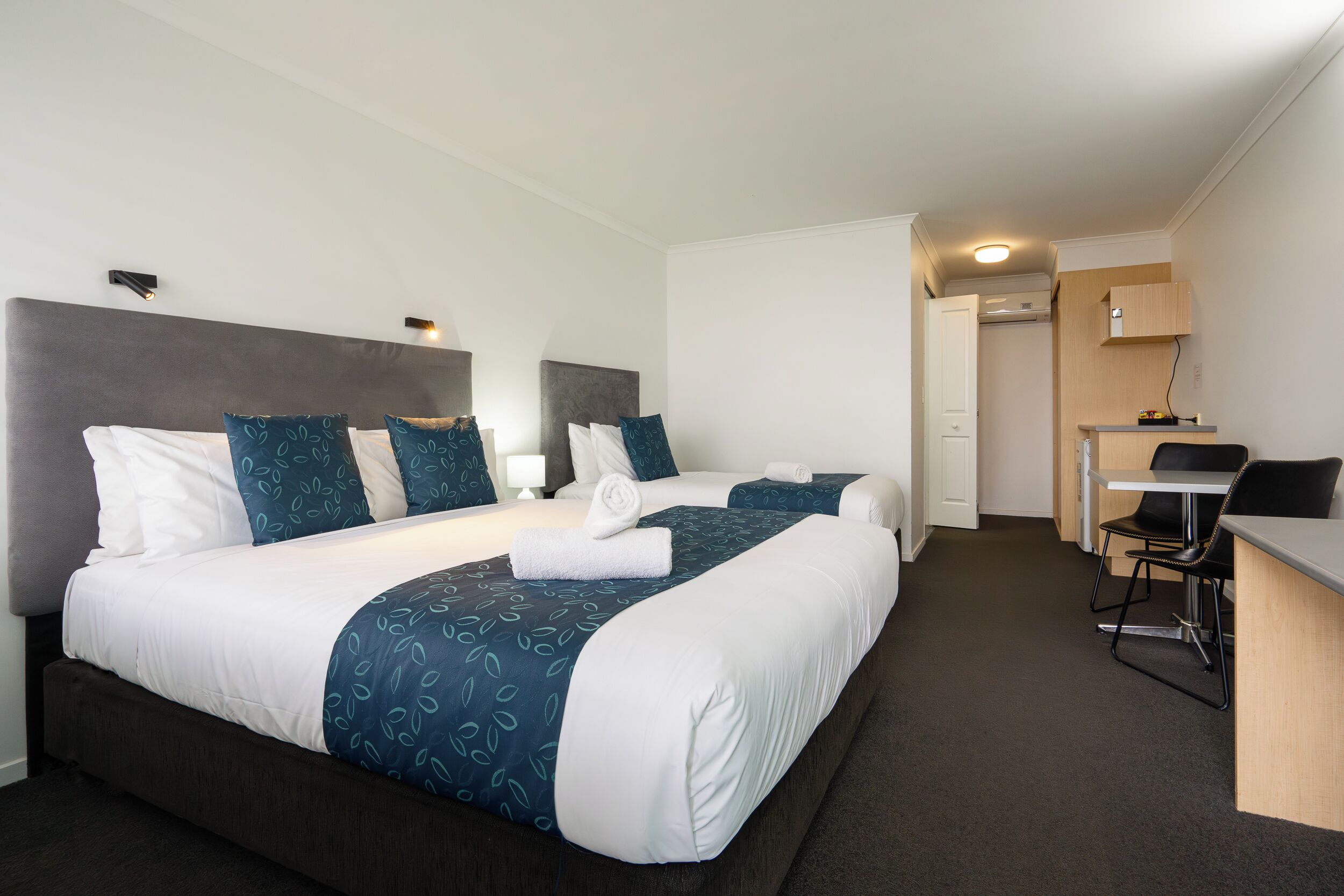 A hotel room with two beds, a desk, and a chair.