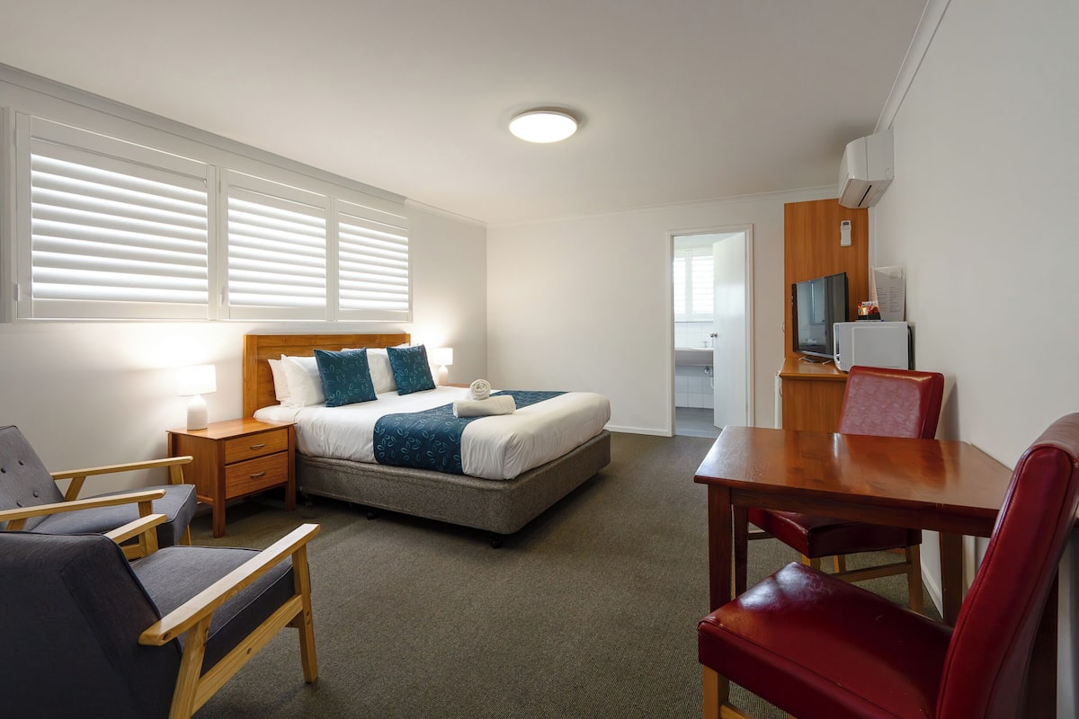 A hotel room with a bed, bedside tables, a desk, and chairs.