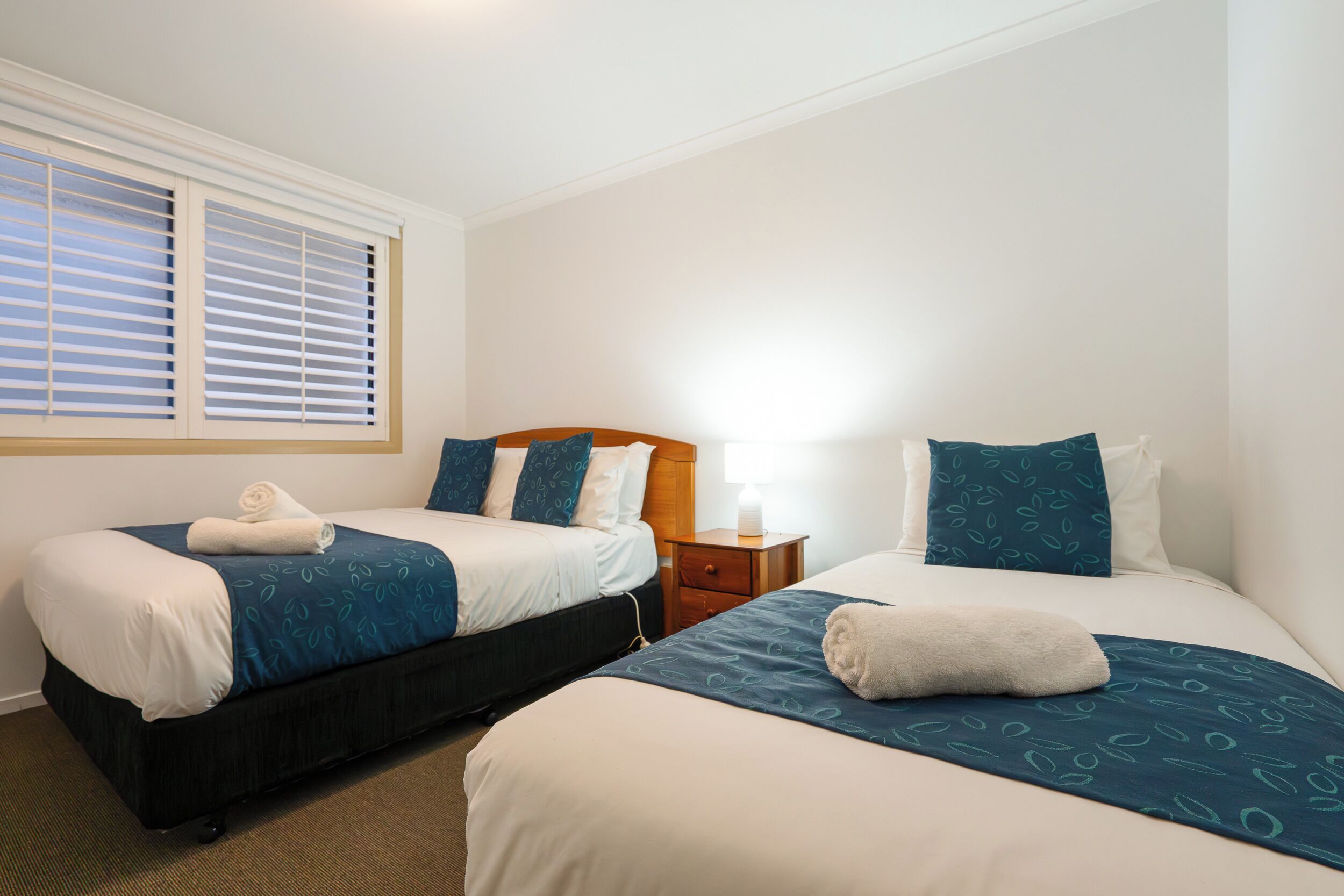 A hotel room with two beds, a nightstand, and a window with blinds.