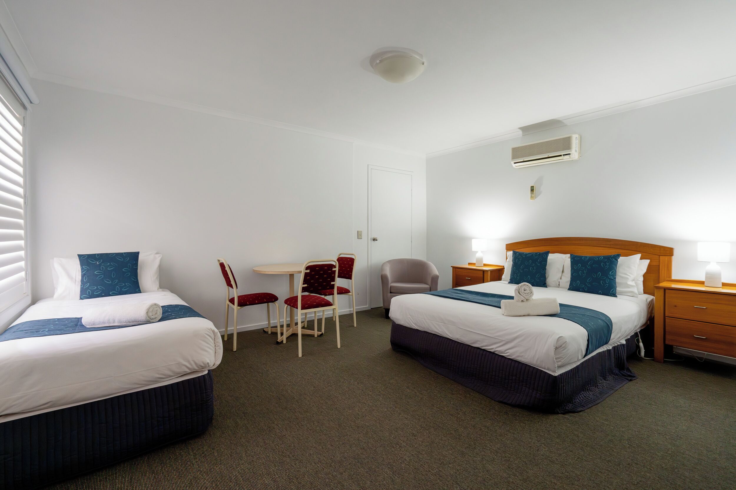A hotel room with two beds, a small table, two chairs, a desk, and a nightstand.