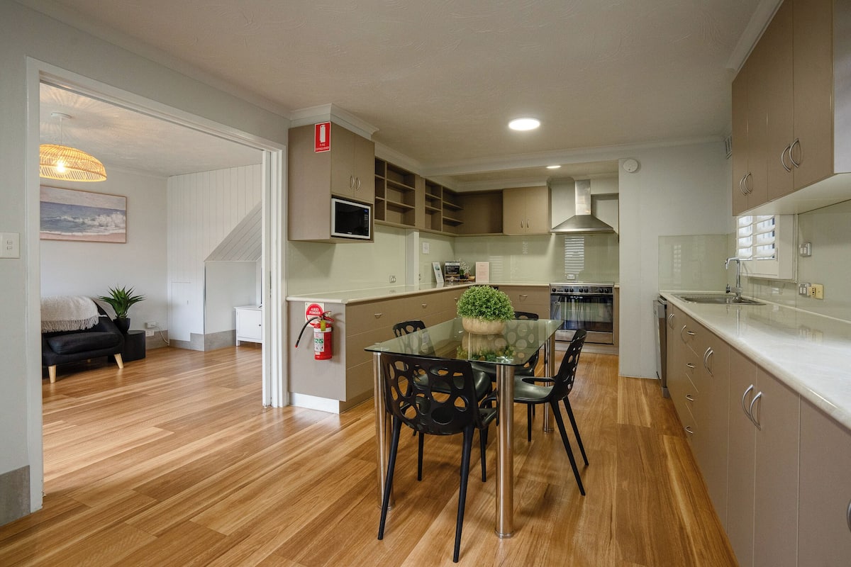 A modern kitchen with wooden flooring, a glass dining table, and built-in cabinets.