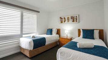A hotel room with two beds, a nightstand, a lamp, and a window with blinds.