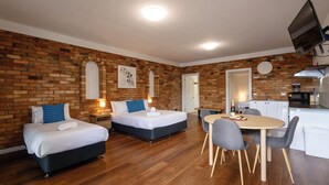 A modern room with two beds, a dining table, and a kitchen area.