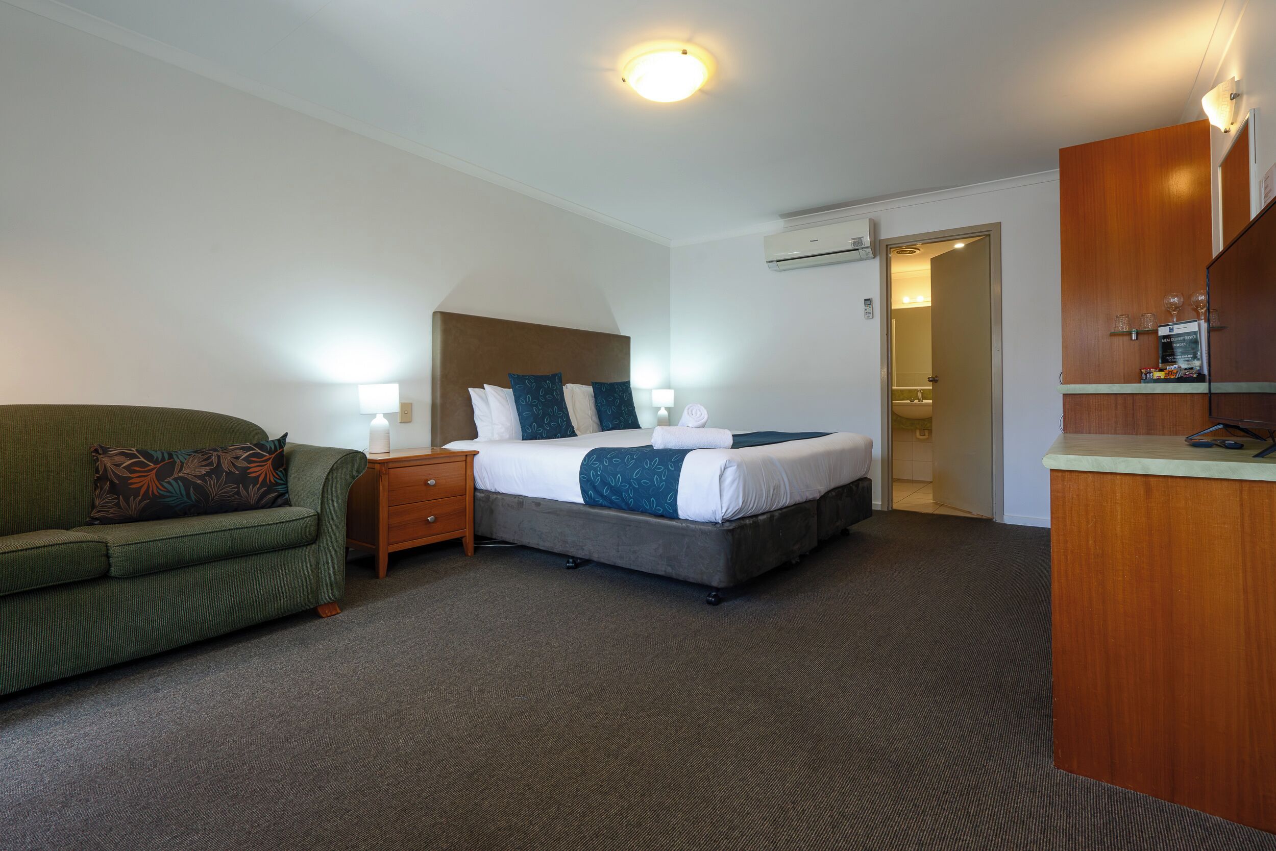 Een hotelkamer met een bed, een groene bank, een houten nachtkastje en een bureau met een spiegel.