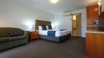 Een hotelkamer met een bed, een groene bank, een houten nachtkastje en een bureau met een spiegel.