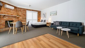A modern living room with a brick wall, a sofa, a dining table with chairs, and a fireplace.