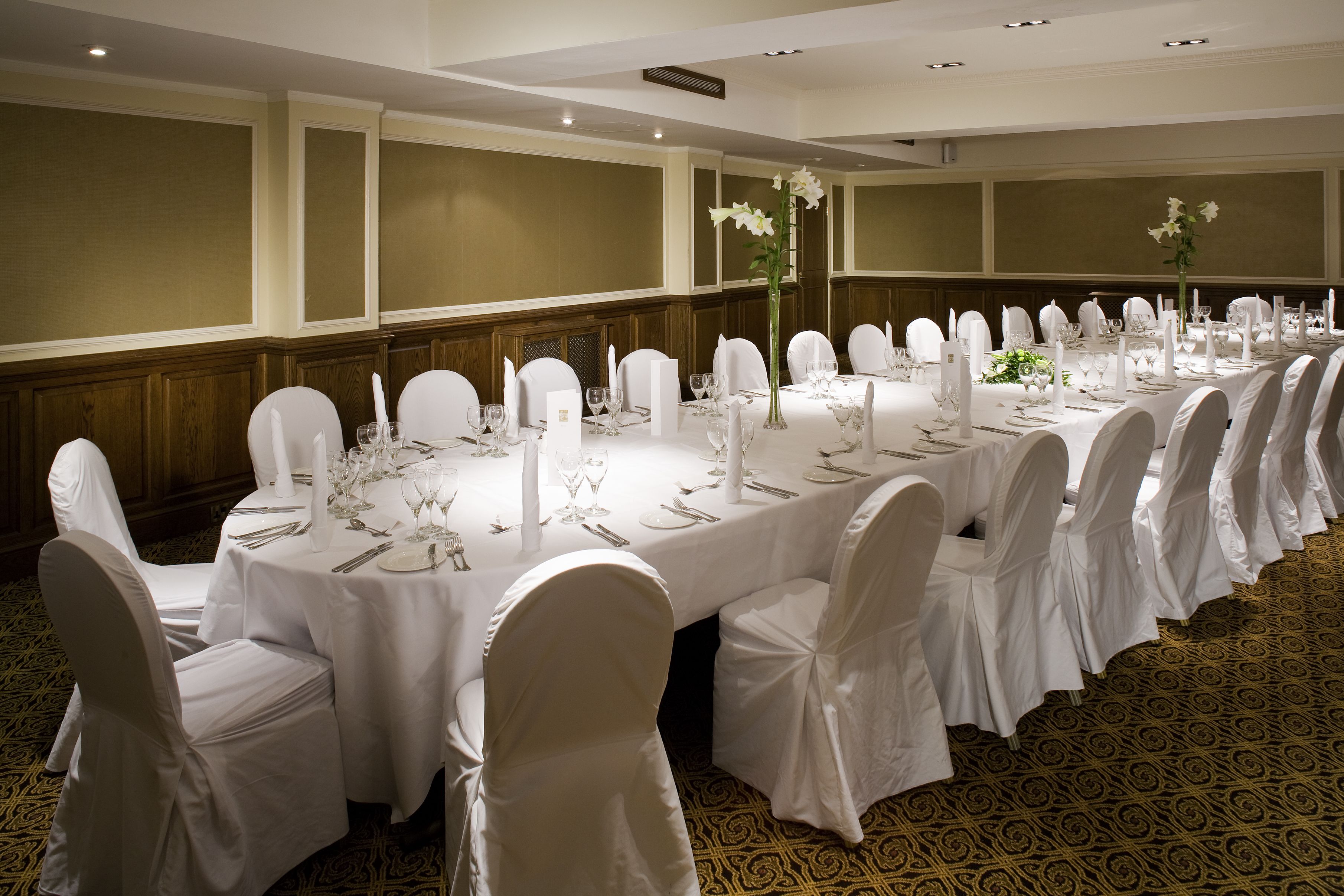 Une salle de banquet avec des tables rondes dressées pour le repas, des chaises blanches et des centres de table floraux.