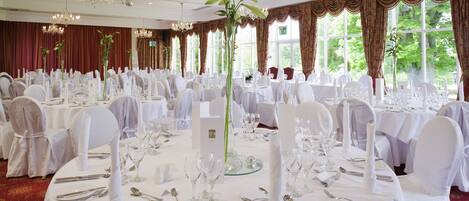 A banquet hall with round tables set for a formal event, featuring white tablecloths, silverware, and glassware.