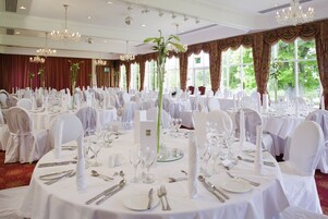 A banquet hall with round tables set for a formal event, featuring white tablecloths, silverware, and glassware.