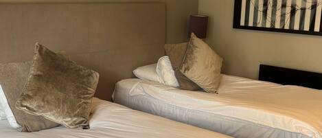 A hotel room with two beds, each with white linens and multiple pillows. There are framed pictures on the wall above the beds.