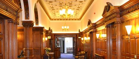 A grand hallway with ornate wood paneling, a chandelier, and a carpet with a tree design.