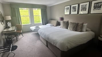 Ein Hotelzimmer mit einem großen Bett, einem Schreibtisch mit Stuhl, einem kleinen Tisch und einem Fenster mit Vorhängen.