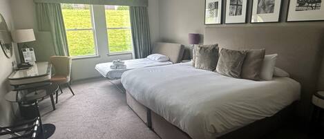 A hotel room with a large bed, a desk with a chair, a small table, and a window with curtains.