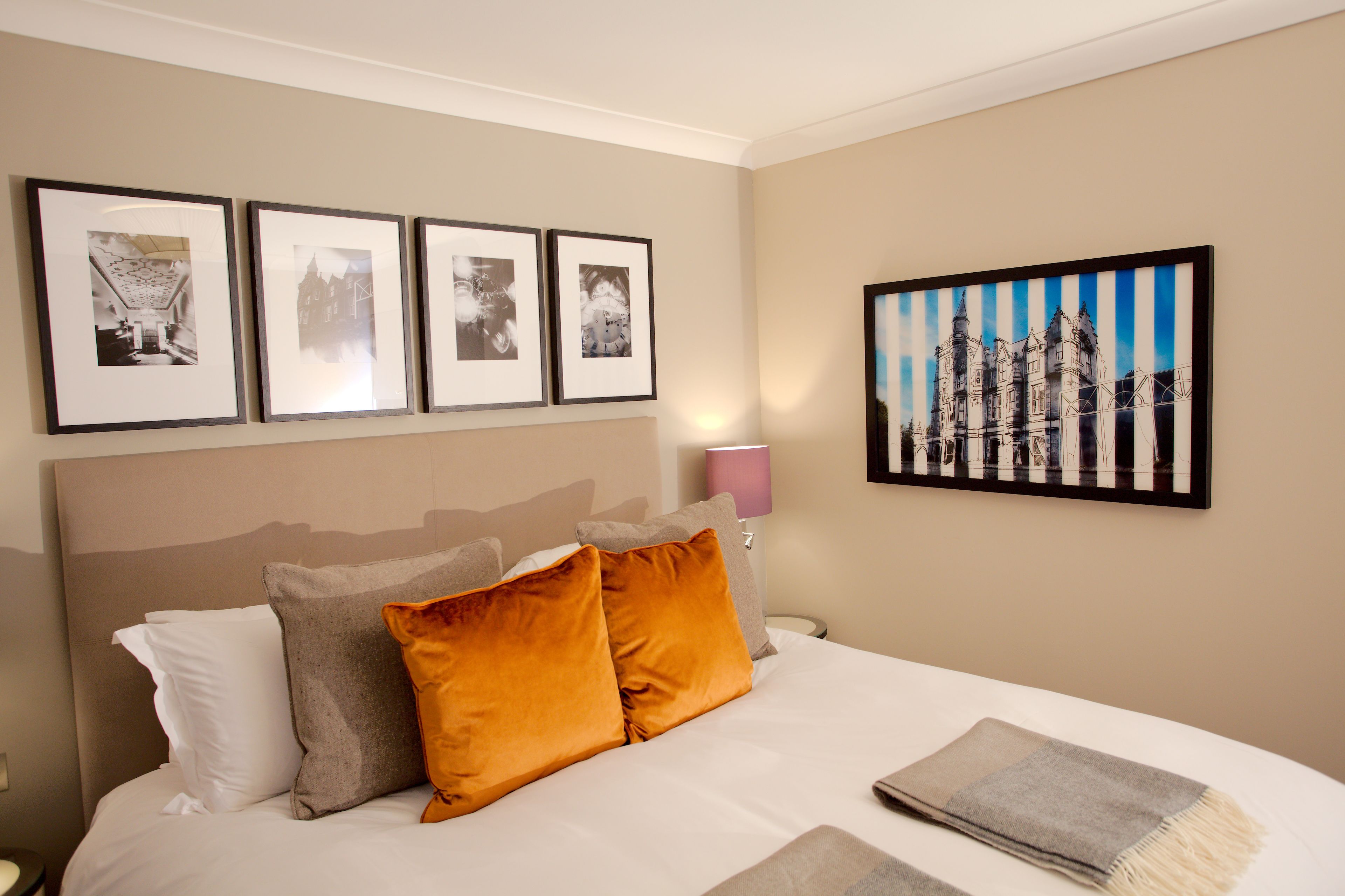 A hotel room with a bed, pillows, a lamp, and framed pictures on the wall.