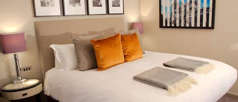 A neatly made bed with pillows, a bedside lamp, and framed pictures on the wall.