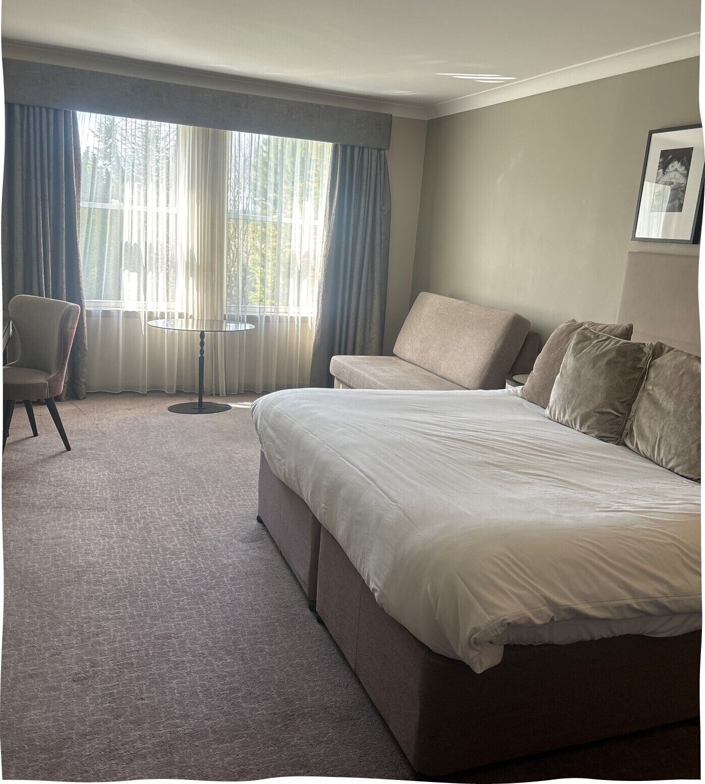 Habitación de hotel con una cama grande, una silla, una mesita y una ventana con cortinas.