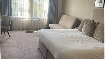 A hotel room with a large bed, a chair, a small table, and a window with curtains.