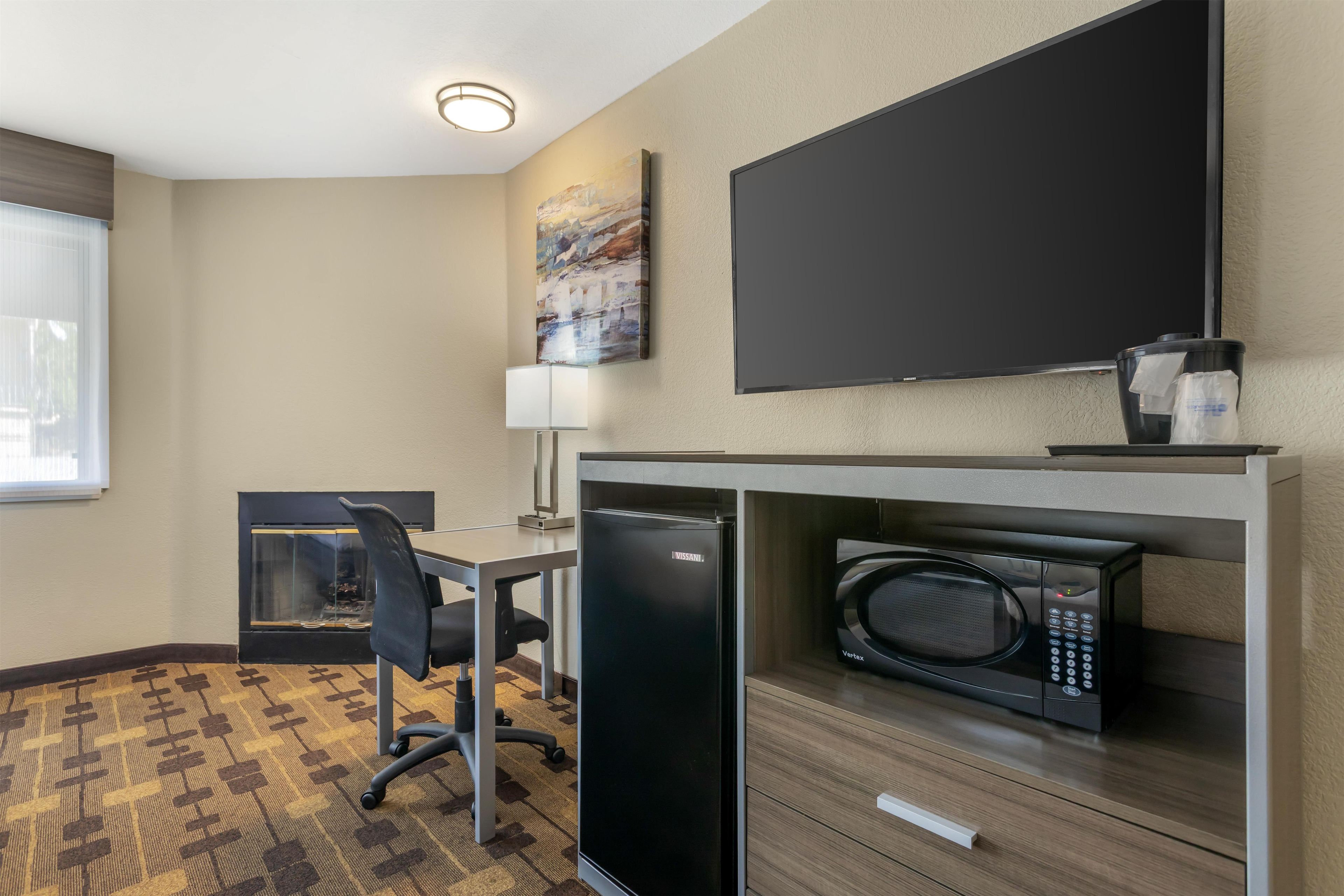 A hotel room with a desk, chair, microwave, and a flat-screen TV mounted on the wall.
