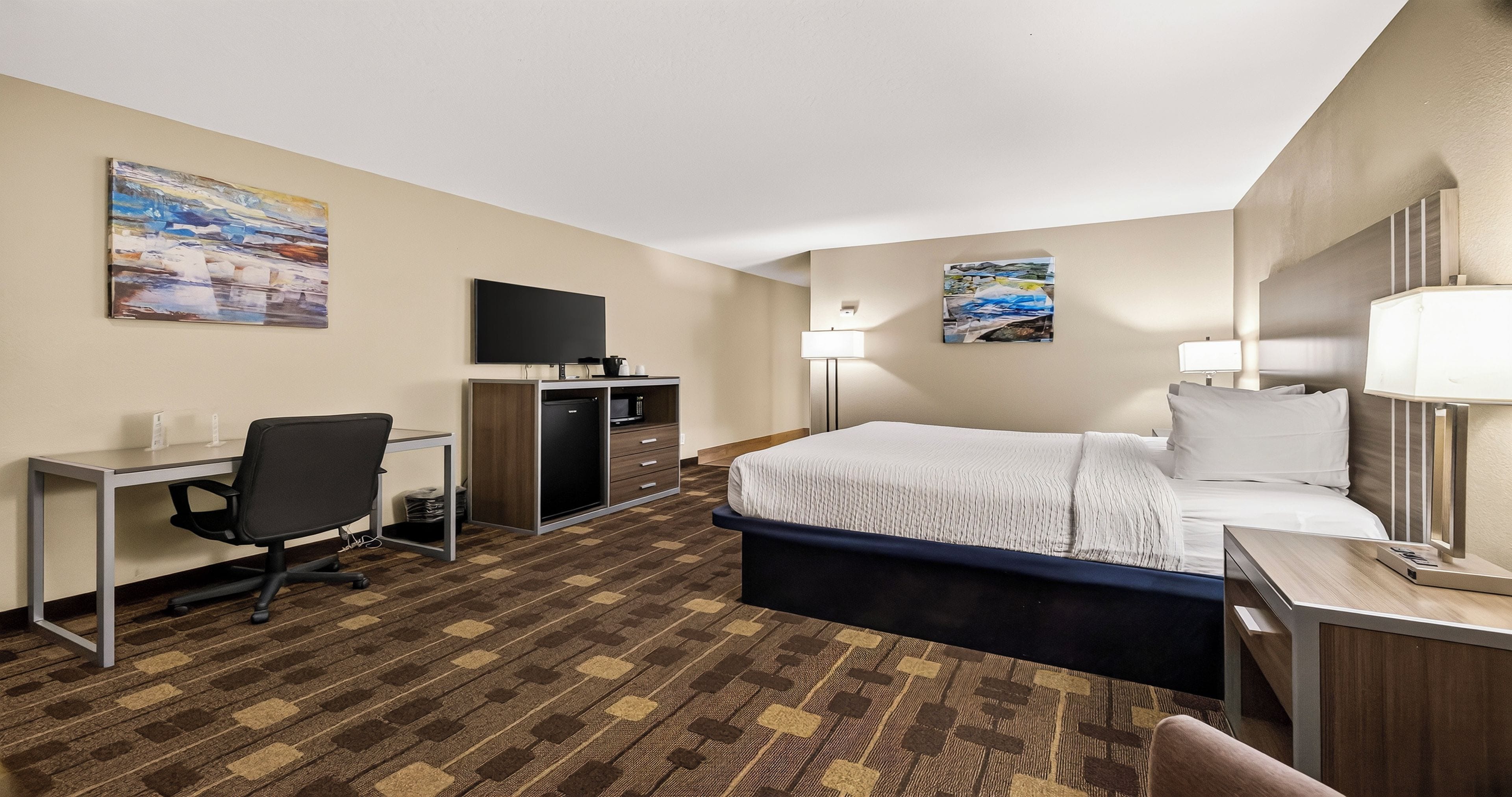 Ein Hotelzimmer mit Bett, Schreibtisch, Stuhl, Fernseher und Bildern an den Wänden.