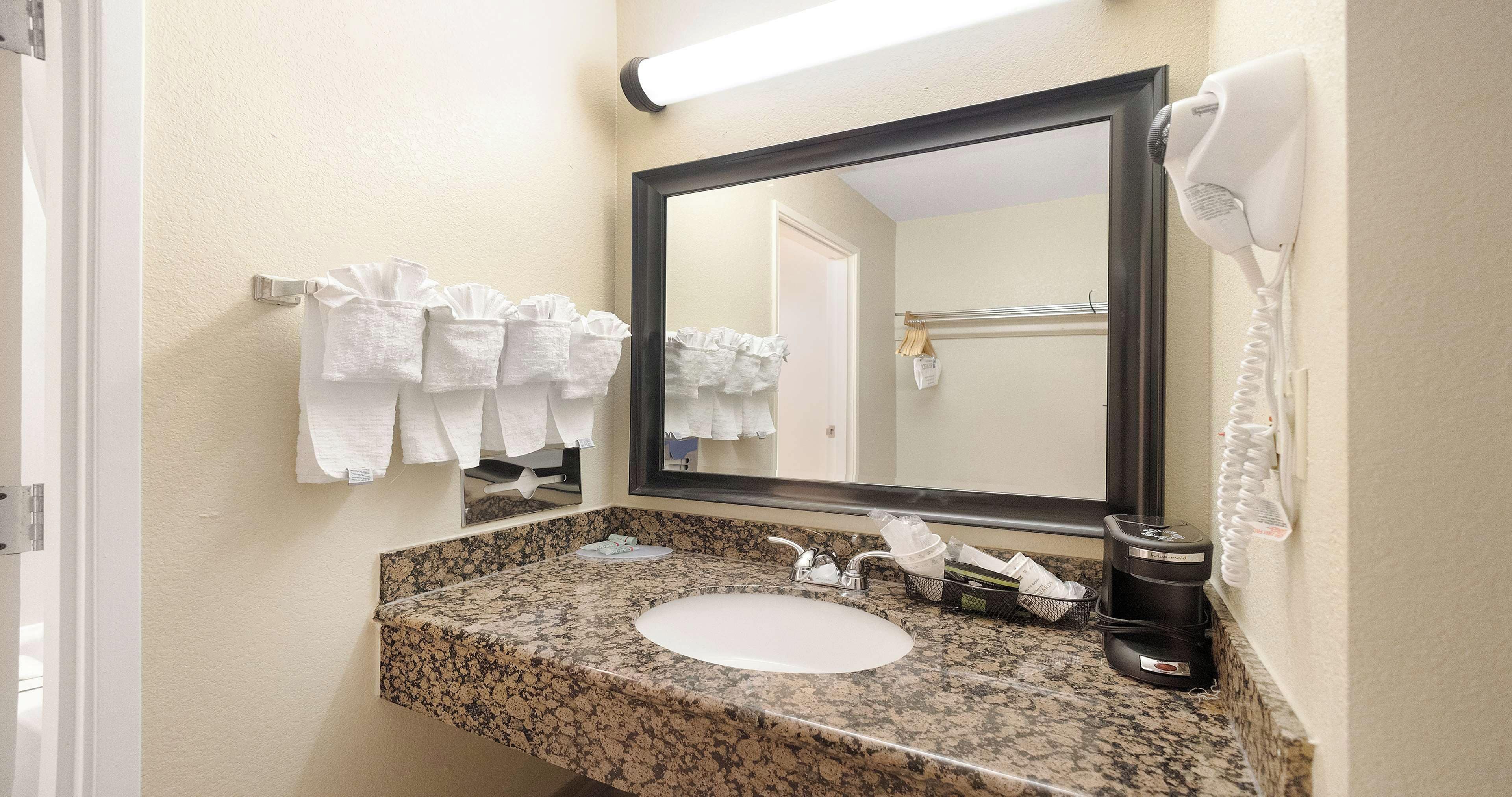 A bathroom with a granite countertop, a sink, a mirror, and a hairdryer mounted on the wall.