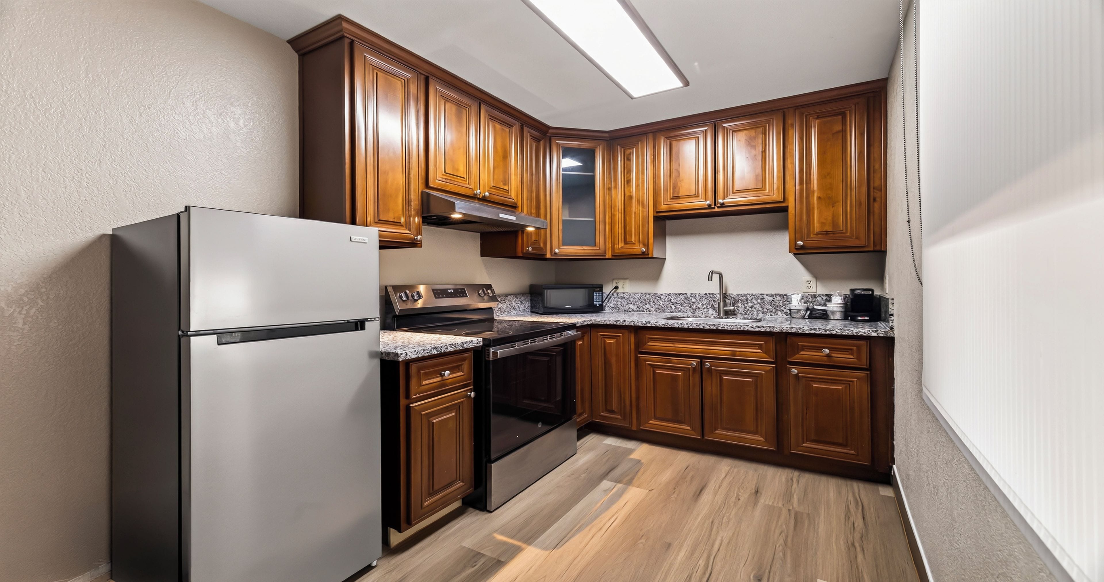 A kitchen with wooden cabinets, a stainless steel refrigerator, a microwave, and a granite countertop.