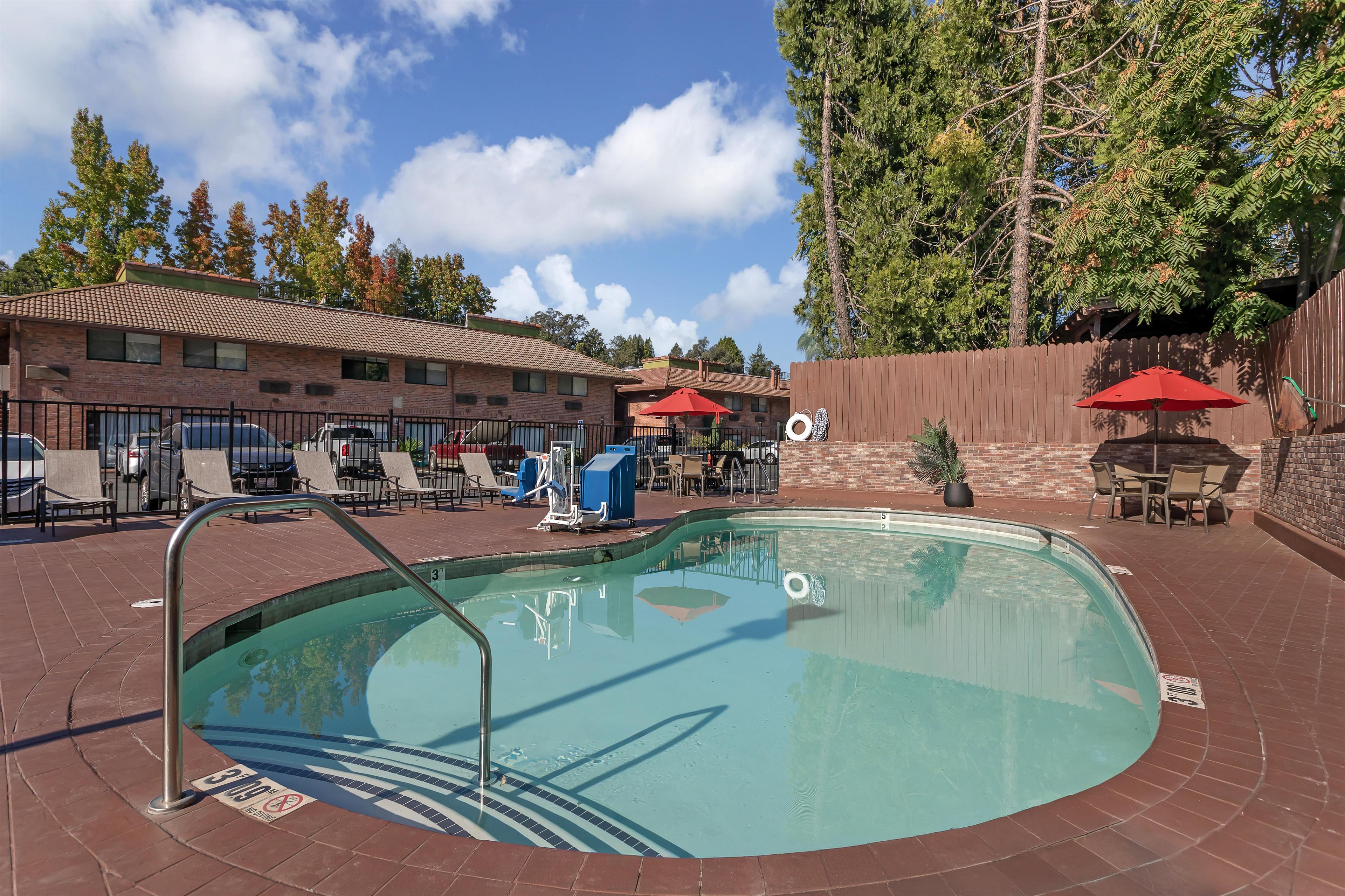 A swimming pool with lounge chairs and umbrellas, surrounded by a brick building with a tiled roof.