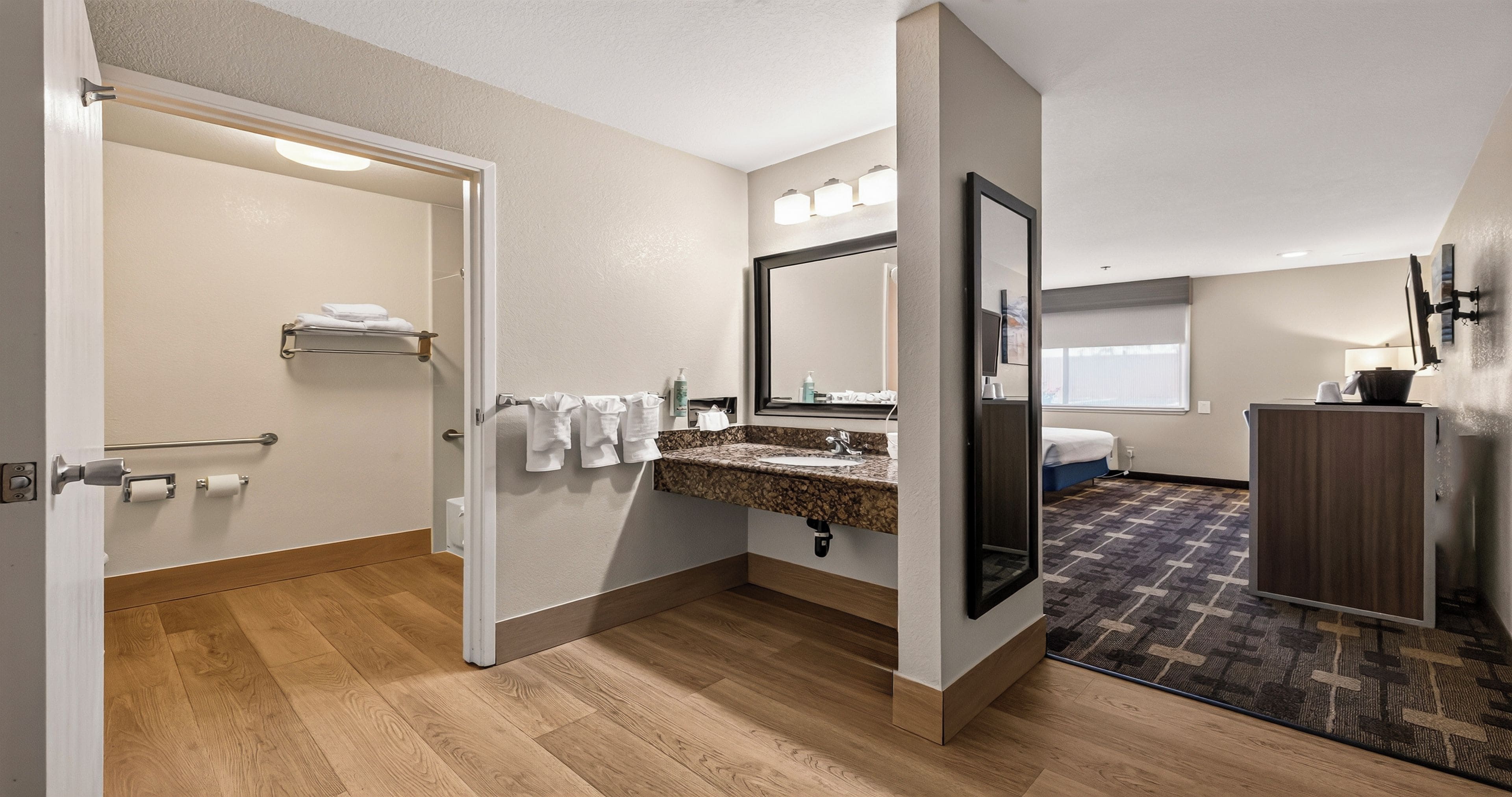 A modern bathroom with a wooden floor, a sink with a marble countertop, a large mirror, and a towel rack.
